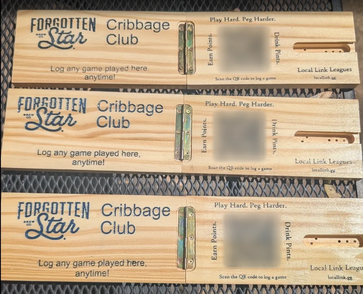Three hinged wooden cribbage boards laser-engraved with the Forgotten Star logo, Cribbage Club, Log any game played here anytime, and a QR code
