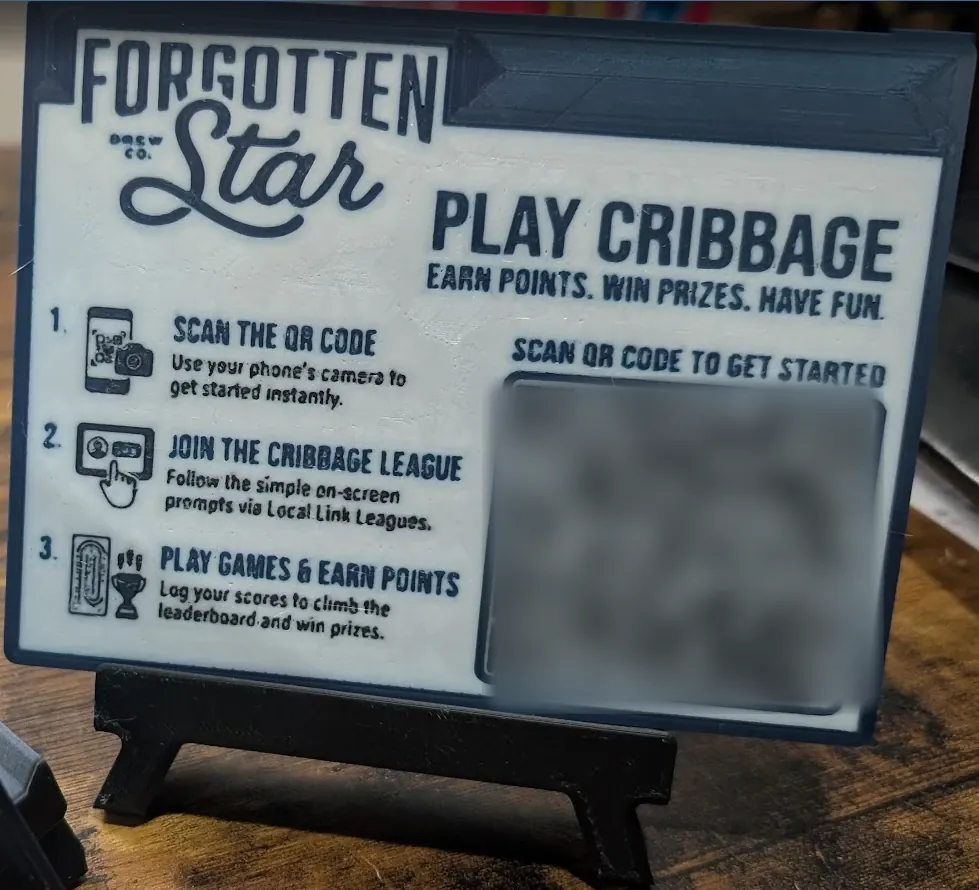 A 3D-printed Forgotten Star table sign on a small easel: Play Cribbage. Earn points. Win prizes. Have fun. Three steps and a QR code
