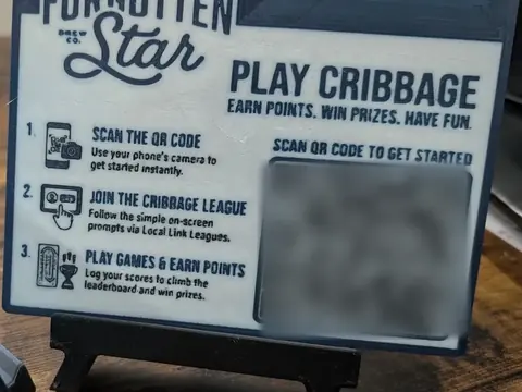 A 3D-printed Forgotten Star table sign on a small easel: Play Cribbage. Earn points. Win prizes. Have fun. Three steps and a QR code